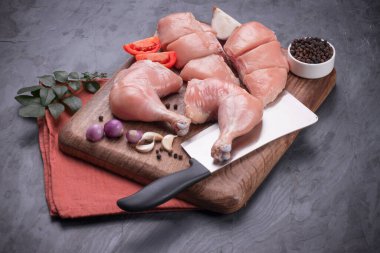 Taze derisiz çiğ tavuk bacakları, bagetler ve çiğ tavuk göğsü kahverengi ahşap bir tabanda gri desenli arka planda..