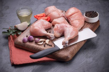 Taze derisiz çiğ tavuk bacakları, bagetler ve çiğ tavuk göğsü kahverengi ahşap bir tabanda gri desenli arka planda..