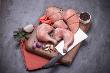 Taze derisiz çiğ tavuk bacakları, bagetler ve çiğ tavuk göğsü kahverengi ahşap bir tabanda gri desenli arka planda..