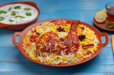 Hydrabadi Tavuk Biryani veya Basmathi pilavlı Tandoori tavuğu ve raita veya raitha meze olarak ve sıcak limon çayı mavi arkaplan veya desenli, seçici odaklı