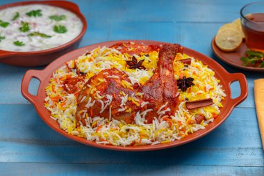 Hydrabadi Tavuk Biryani veya Basmathi pilavlı Tandoori tavuğu ve raita veya raitha meze olarak ve sıcak limon çayı mavi arkaplan veya desenli, seçici odaklı