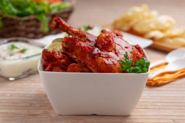 Baharatlı Tandır tavuğu kişniş yaprağıyla süslenmiş kare şeklinde beyaz kâse içinde sebzeli pulav, raita ve paapad ve ahşap desenli, seçici odaklı.