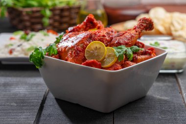 Limon ve kişniş yaprağıyla süslenmiş tandır tavuğu kare şeklinde beyaz kâse içinde sebzeli pulav, raita ve paapad ile siyah desenli, seçici odaklı.