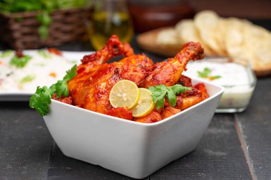 Limon ve kişniş yaprağıyla süslenmiş tandır tavuğu kare şeklinde beyaz kâse içinde sebzeli pulav, raita ve paapad ile siyah desenli, seçici odaklı.