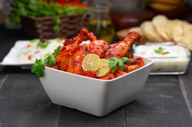 Limon ve kişniş yaprağıyla süslenmiş tandır tavuğu kare şeklinde beyaz kâse içinde sebzeli pulav, raita ve paapad ile siyah desenli, seçici odaklı.