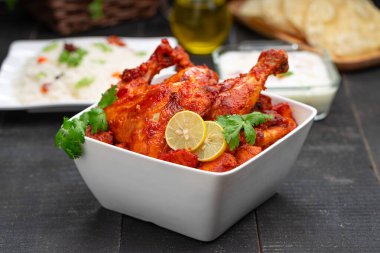 Limon ve kişniş yaprağıyla süslenmiş tandır tavuğu kare şeklinde beyaz kâse içinde sebzeli pulav, raita ve paapad ile siyah desenli, seçici odaklı.