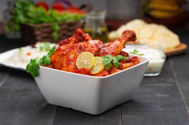 Limon ve kişniş yaprağıyla süslenmiş tandır tavuğu kare şeklinde beyaz kâse içinde sebzeli pulav, raita ve paapad ile siyah desenli, seçici odaklı.