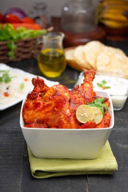 Limon ve kişniş yaprağıyla süslenmiş tandır tavuğu kare şeklinde beyaz kâse içinde sebzeli pulav, raita ve paapad ile siyah desenli, seçici odaklı.