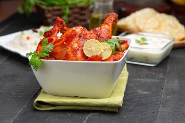 Limon ve kişniş yaprağıyla süslenmiş tandır tavuğu kare şeklinde beyaz kâse içinde sebzeli pulav, raita ve paapad ile siyah desenli, seçici odaklı.