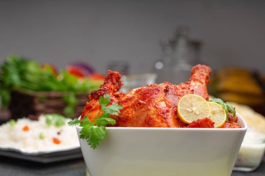 Limon ve kişniş yaprağıyla süslenmiş tandır tavuğu kare şeklinde beyaz kâse içinde sebzeli pulav, raita ve paapad ile siyah desenli, seçici odaklı.