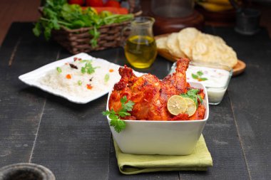 Limon ve kişniş yaprağıyla süslenmiş tandır tavuğu kare şeklinde beyaz kâse içinde sebzeli pulav, raita ve paapad ile siyah desenli, seçici odaklı.