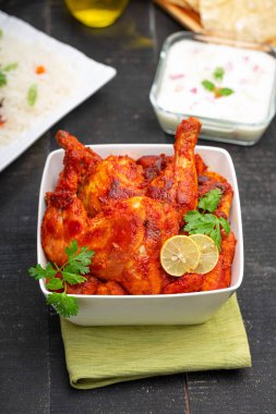 Limon ve kişniş yaprağıyla süslenmiş tandır tavuğu kare şeklinde beyaz kâse içinde sebzeli pulav, raita ve paapad ile siyah desenli, seçici odaklı.