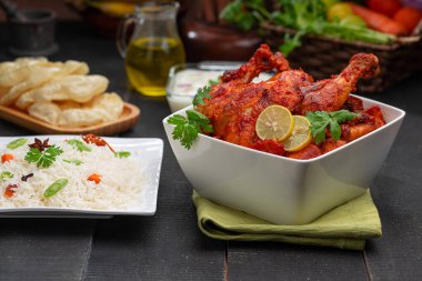 Limon ve kişniş yaprağıyla süslenmiş tandır tavuğu kare şeklinde beyaz kâse içinde sebzeli pulav, raita ve paapad ile siyah desenli, seçici odaklı.