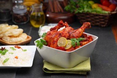 Limon ve kişniş yaprağıyla süslenmiş tandır tavuğu kare şeklinde beyaz kâse içinde sebzeli pulav, raita ve paapad ile siyah desenli, seçici odaklı.