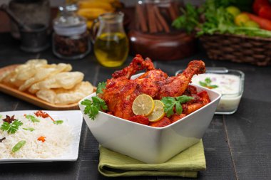 Limon ve kişniş yaprağıyla süslenmiş tandır tavuğu kare şeklinde beyaz kâse içinde sebzeli pulav, raita ve paapad ile siyah desenli, seçici odaklı.