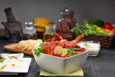 Limon ve kişniş yaprağıyla süslenmiş tandır tavuğu kare şeklinde beyaz kâse içinde sebzeli pulav, raita ve paapad ile siyah desenli, seçici odaklı.