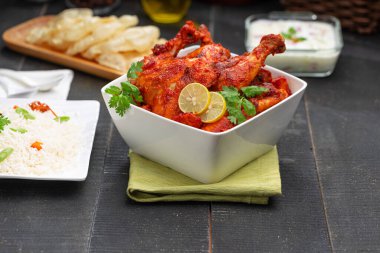 Limon ve kişniş yaprağıyla süslenmiş tandır tavuğu kare şeklinde beyaz kâse içinde sebzeli pulav, raita ve paapad ile siyah desenli, seçici odaklı.