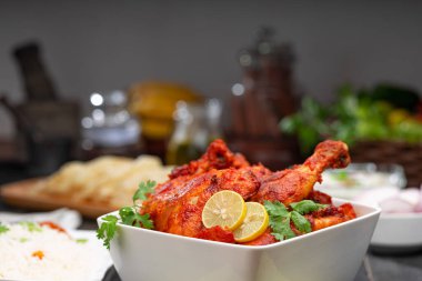 Limon ve kişniş yaprağıyla süslenmiş tandır tavuğu kare şeklinde beyaz kâse içinde sebzeli pulav, raita ve paapad ile siyah desenli, seçici odaklı.