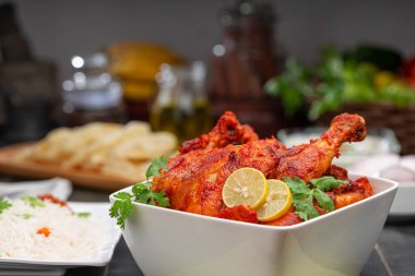 Limon ve kişniş yaprağıyla süslenmiş tandır tavuğu kare şeklinde beyaz kâse içinde sebzeli pulav, raita ve paapad ile siyah desenli, seçici odaklı.