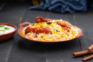 Mandi Biryani tavuğu, Tandır tavuğu, Hydrabadi tavuk biryani basmathi pilavı ve raita ya da raitha ile siyah arkaplan ya da desenli bir toprak takımında servis edilmiş, seçici odak noktası