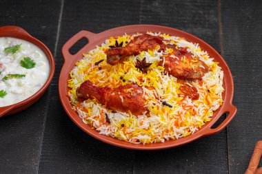Mandi Biryani tavuğu, Tandır tavuğu, Hydrabadi tavuk biryani basmathi pilavı ve raita ya da raitha ile siyah arkaplan ya da desenli bir toprak takımında servis edilmiş, seçici odak noktası