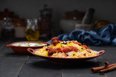 Mandi Biryani tavuğu, Tandır tavuğu, Hydrabadi tavuk biryani basmathi pilavı ve raita ya da raitha ile siyah arkaplan ya da desenli bir toprak takımında servis edilmiş, seçici odak noktası