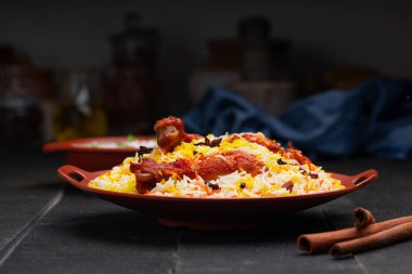 Mandi Biryani tavuğu, Tandır tavuğu, Hydrabadi tavuk biryani basmathi pilavı ve raita ya da raitha ile siyah arkaplan ya da desenli bir toprak takımında servis edilmiş, seçici odak noktası