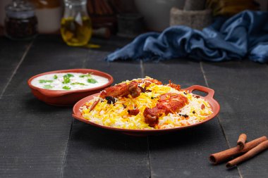 Mandi Biryani tavuğu, Tandır tavuğu, Hydrabadi tavuk biryani basmathi pilavı ve raita ya da raitha ile siyah arkaplan ya da desenli bir toprak takımında servis edilmiş, seçici odak noktası