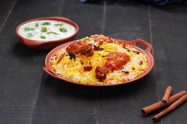 Mandi Biryani tavuğu, Tandır tavuğu, Hydrabadi tavuk biryani basmathi pilavı ve raita ya da raitha ile siyah arkaplan ya da desenli bir toprak takımında servis edilmiş, seçici odak noktası