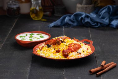 Mandi Biryani tavuğu, Tandır tavuğu, Hydrabadi tavuk biryani basmathi pilavı ve raita ya da raitha ile siyah arkaplan ya da desenli bir toprak takımında servis edilmiş, seçici odak noktası