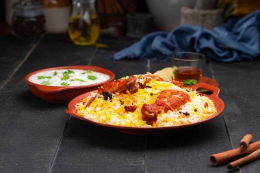 Mandi Biryani tavuğu, Tandır tavuğu, Hydrabadi tavuk biryani basmathi pilavı ve raita yanında siyah arkaplan ve desenli bir toprak tabaktaki sıcak limon çayı, seçici odak noktası.