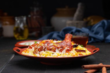 Mandi Biryani tavuğu, Tandır tavuğu, Hydrabadi tavuk biryani basmathi pilavı ve raita yanında siyah arkaplan ve desenli bir toprak tabaktaki sıcak limon çayı, seçici odak noktası.