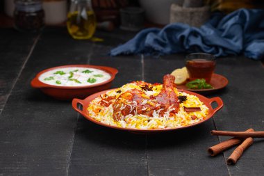 Mandi Biryani tavuğu, Tandır tavuğu, Hydrabadi tavuk biryani basmathi pilavı ve raita yanında siyah arkaplan ve desenli bir toprak tabaktaki sıcak limon çayı, seçici odak noktası.