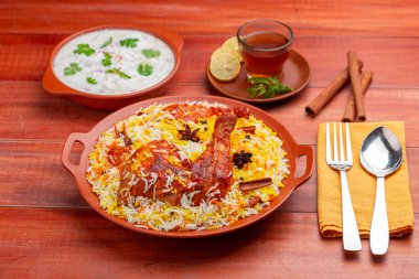 Tavuk dum biryani, Hydrabadi tavuk biryani ile basmathi pilavı ve raita yan yemek olarak ve ahşap arka planda veya dokuda sıcak limon çayı, seçici odak noktası