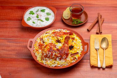 Tavuk dum biryani, Hydrabadi tavuk biryani ile basmathi pilavı ve raita yan yemek olarak ve ahşap arka planda veya dokuda sıcak limon çayı, seçici odak noktası