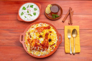 Tavuk dum biryani 'nin üst görüntüsü, basmathi pilavlı tavuk biryani ve raita meze olarak ve ahşap arkaplan veya dokuya sahip sıcak limon çayı, seçici odaklı.