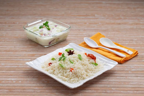 Veg Pulav or Pulao, made using basmathi rice ,vegetables and indian spices.Raita as side dish arranged in a square white tableware with wooden colour background or texture