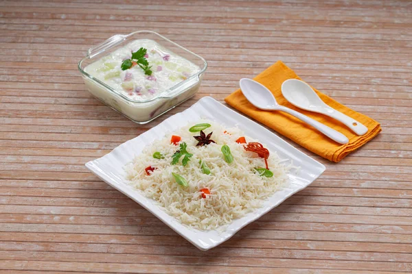 Veg Pulav or Pulao, made using basmathi rice ,vegetables and indian spices.Raita as side dish arranged in a square white tableware with wooden colour background or texture