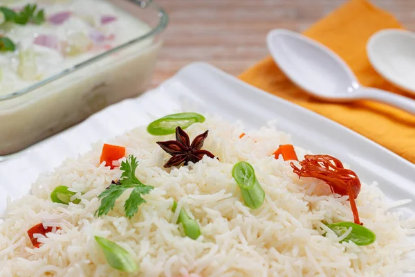 Veg Pulav or Pulao, made using basmathi rice ,vegetables and indian spices.Raita as side dish arranged in a square white tableware with wooden colour background or texture