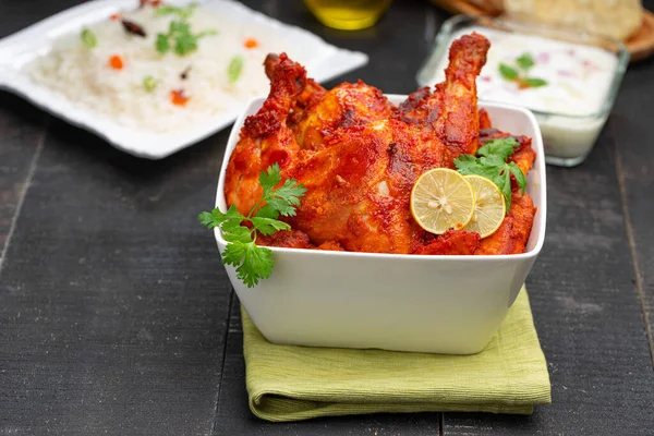 Limon ve kişniş yaprağıyla süslenmiş tandır tavuğu kare şeklinde beyaz kâse içinde sebzeli pulav, raita ve paapad ile siyah desenli, seçici odaklı.