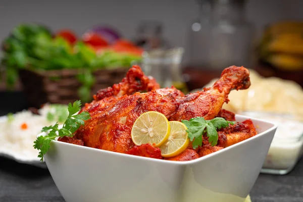 Limon ve kişniş yaprağıyla süslenmiş tandır tavuğu kare şeklinde beyaz kâse içinde sebzeli pulav, raita ve paapad ile siyah desenli, seçici odaklı.