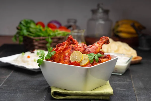 Limon ve kişniş yaprağıyla süslenmiş tandır tavuğu kare şeklinde beyaz kâse içinde sebzeli pulav, raita ve paapad ile siyah desenli, seçici odaklı.