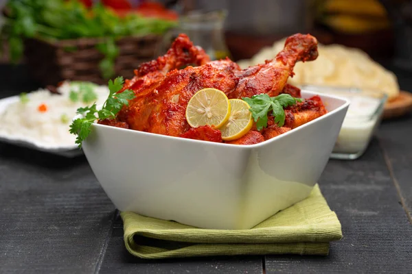 Limon ve kişniş yaprağıyla süslenmiş tandır tavuğu kare şeklinde beyaz kâse içinde sebzeli pulav, raita ve paapad ile siyah desenli, seçici odaklı.