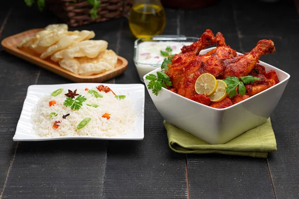 Limon ve kişniş yaprağıyla süslenmiş tandır tavuğu kare şeklinde beyaz kâse içinde sebzeli pulav, raita ve paapad ile siyah desenli, seçici odaklı.