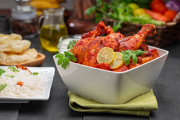 Limon ve kişniş yaprağıyla süslenmiş tandır tavuğu kare şeklinde beyaz kâse içinde sebzeli pulav, raita ve paapad ile siyah desenli, seçici odaklı.