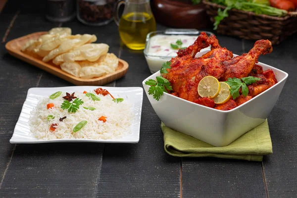 Limon ve kişniş yaprağıyla süslenmiş tandır tavuğu kare şeklinde beyaz kâse içinde sebzeli pulav, raita ve paapad ile siyah desenli, seçici odaklı.