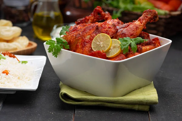 Limon ve kişniş yaprağıyla süslenmiş tandır tavuğu kare şeklinde beyaz kâse içinde sebzeli pulav, raita ve paapad ile siyah desenli, seçici odaklı.