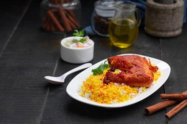 Siyah arkaplan ya da desenli meze olarak tavuk biryani ya da basmathi pilavlı Tandır tavuğu ve raita ya da raitha, seçici odak noktası.