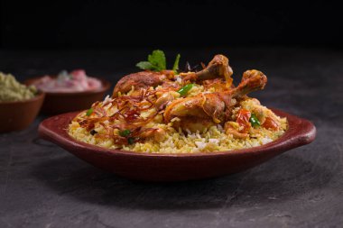 Jeera pilavı ve baharat kullanarak tavuk dhum biryani gri arka planda raitha ve limon turşusu eşliğinde toprak malzemesi..