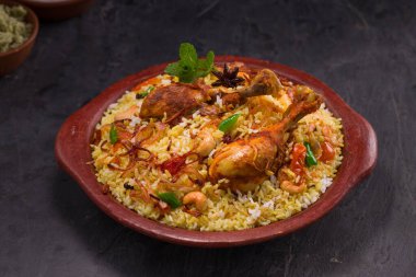 Jeera pilavı ve baharat kullanarak tavuk dhum biryani gri arka planda raitha ve limon turşusu eşliğinde toprak malzemesi..